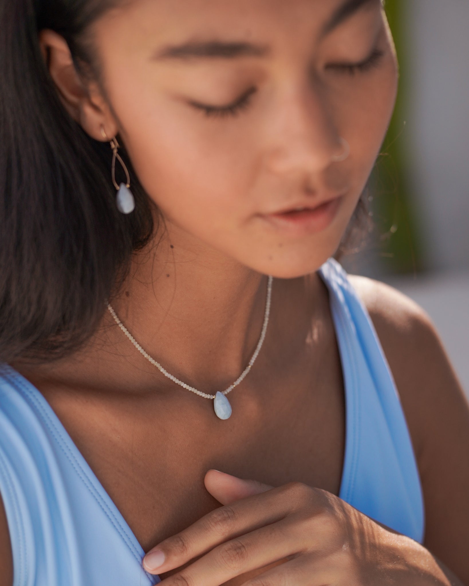 Model wearing a summery gemstone necklace featuring a blue opal tear drop pendant